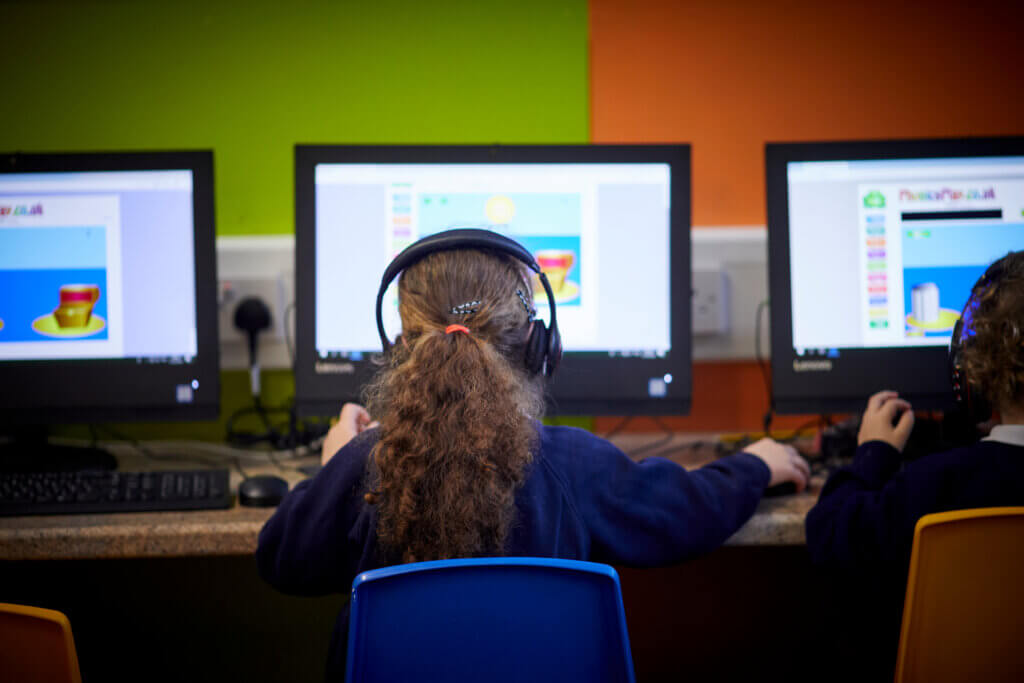A girl sitting in front of a computer in the classroom, wearing headphones.