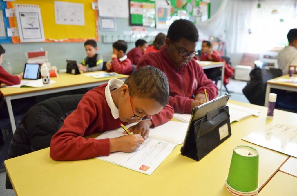 Two boys sitting in front of a tablet, completing written work.