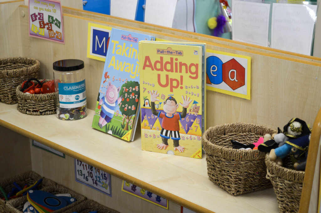 A book shelf in the classroom, with picture books, a jar and a basket with resources.