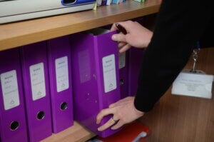 Hands reaching for a ring binder on a shelf.