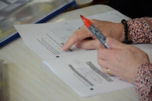 Hands pointing at printed classwork with a red marker pen.