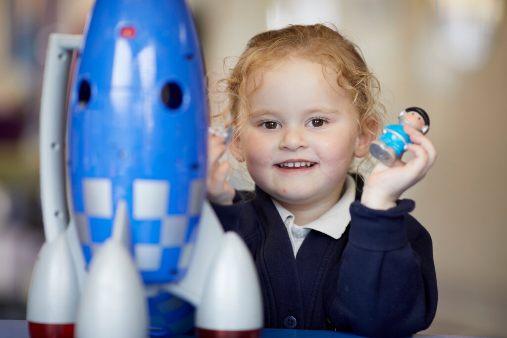 A girl playing with dolls and a toy rocket.