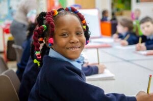 A girl smiling as she holds her pen, writing in the classroom.