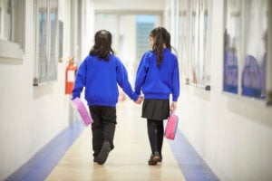 Two girls holding hands in the school hallway.