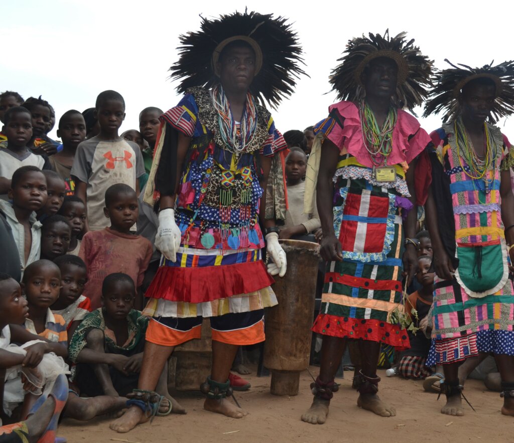 Boys' initiation ceremony gatekeepers dressed in traditional dance costumes in Malawi, surrounded by a group of young boys.