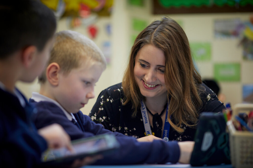 A teacher smiles as she helps a boy in class.