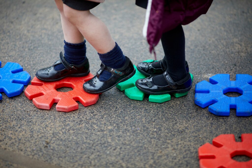 Children's feet walking along colourful plastic stepping stones in the playground.