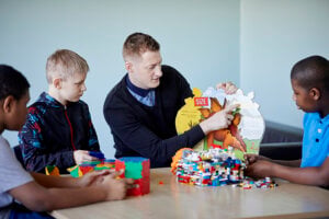 A teacher and three boys sitting around a table, looking at a picture book.