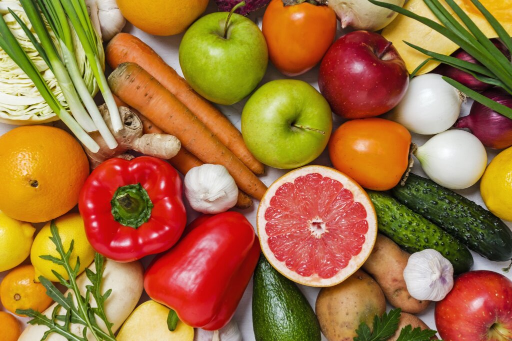 A collection of fruits and vegetables together, including apples, grapefruit, red bell peppers, carrots and potatoes.