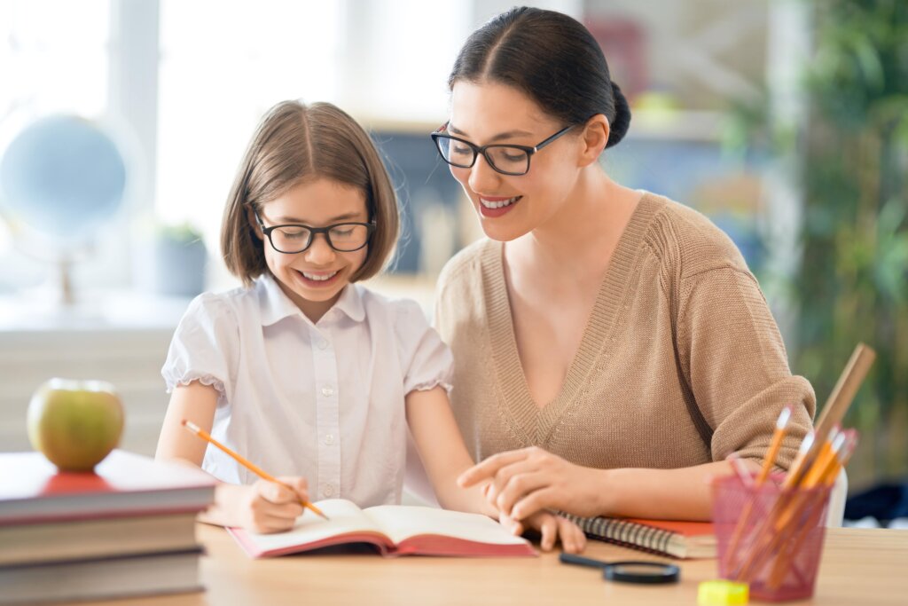 A teacher helping a girl as she writes in her work book.