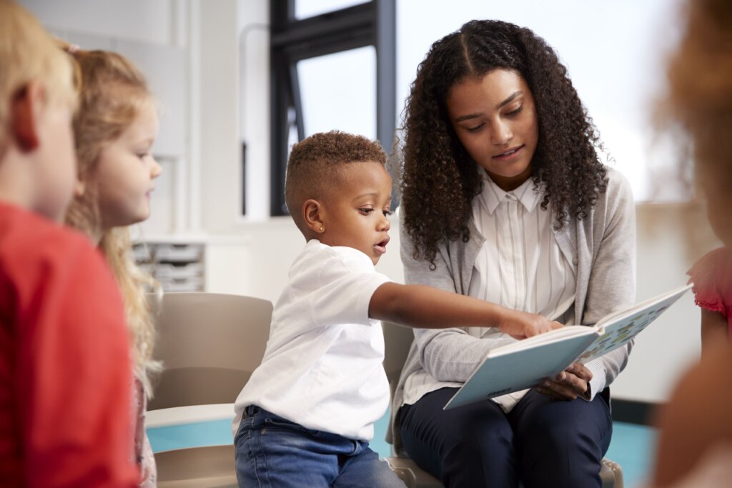 A teacher reading a book to a young boy, who is pointing at the page.