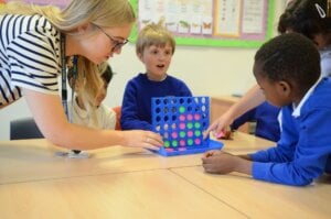 A teacher and a group of pupils playing a game of Connect 4 in the classroom.