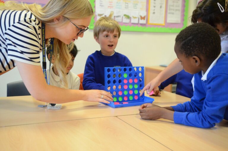 A teacher and a group of pupils playing a game of Connect 4 in the classroom.