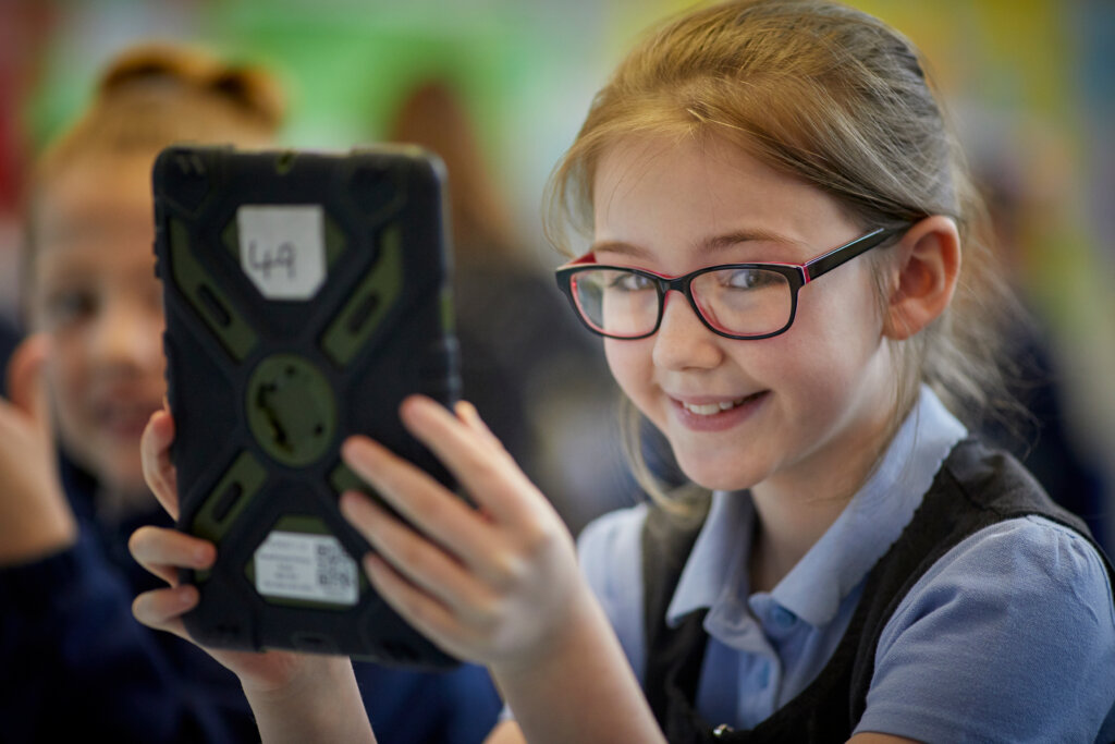 A girl smiles as she holds a tablet in her hands.