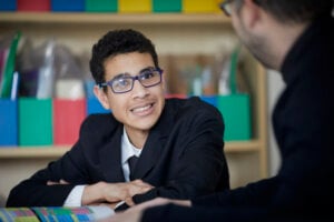 A teenage boy in school uniform, smiling towards his teacher.