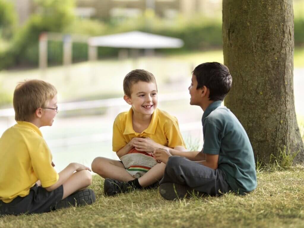 Three boys sitting on the grass outside and laughing together.