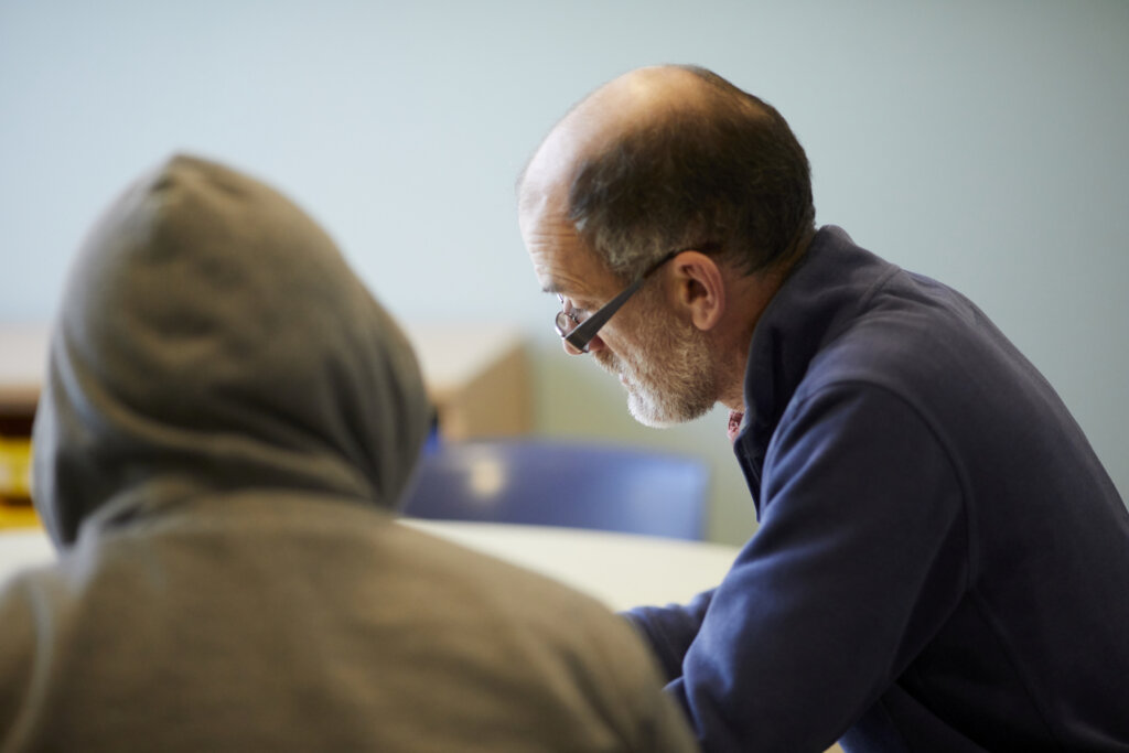 A man and student sitting at a desk together.