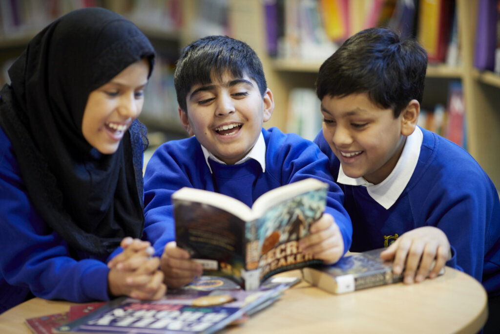 Three children gathered around a table and reading a book together.