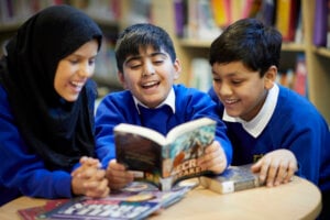 Three children gathered around a table and reading a book together.