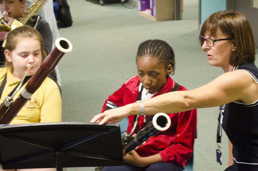 A girl playing the bassoon whilst the teacher points to the sheet music.