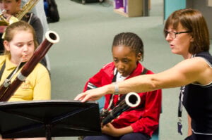 A girl playing the bassoon whilst the teacher points to the sheet music.