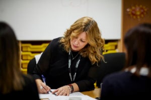 A woman writing notes at a staff meeting.