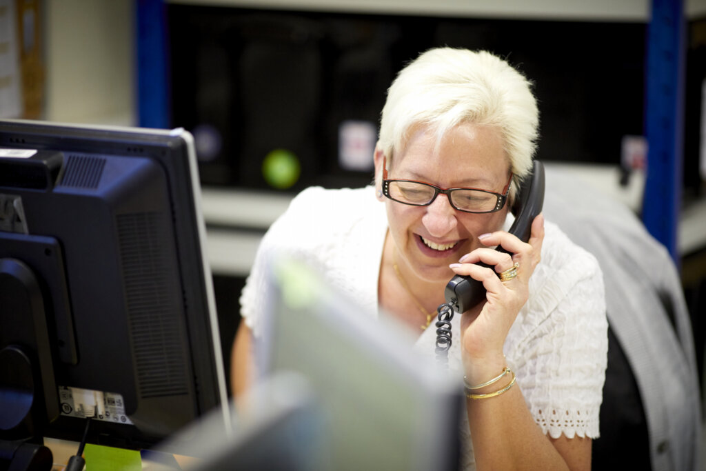 A woman sitting at her computer desk, smiling on the phone.