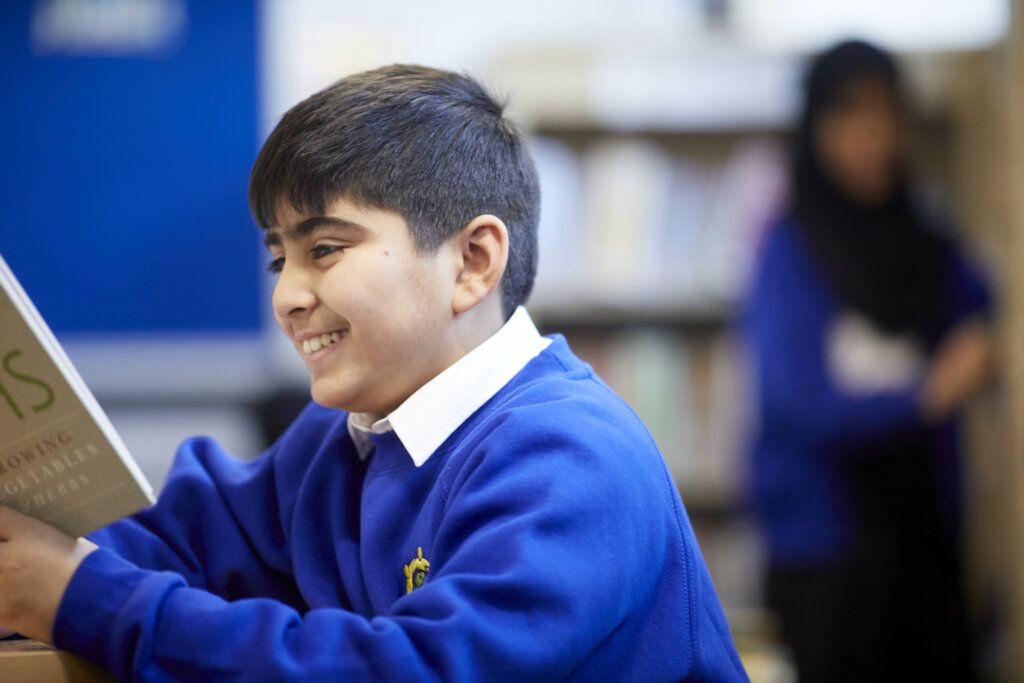 A school boy smiling as he reads his book.