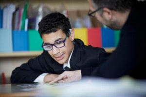 A student looks at something on his desk where his teacher his pointing.
