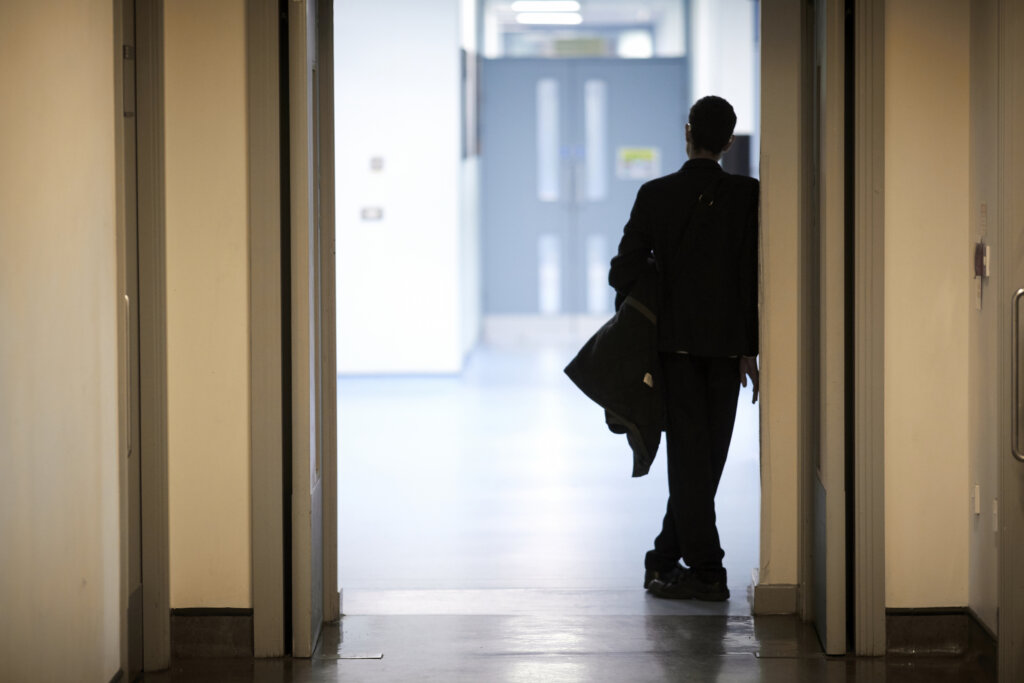 The silhouette of a teenage boy leaning against the wall in a school corridor.