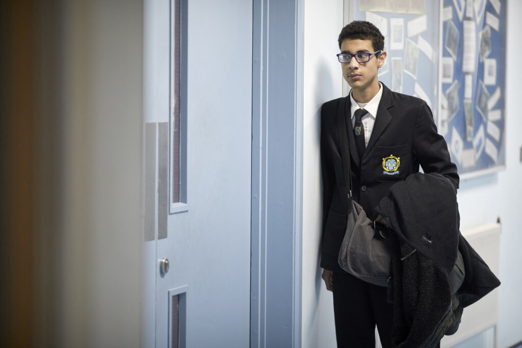 A teenage boy in a school uniform working through the corridor.