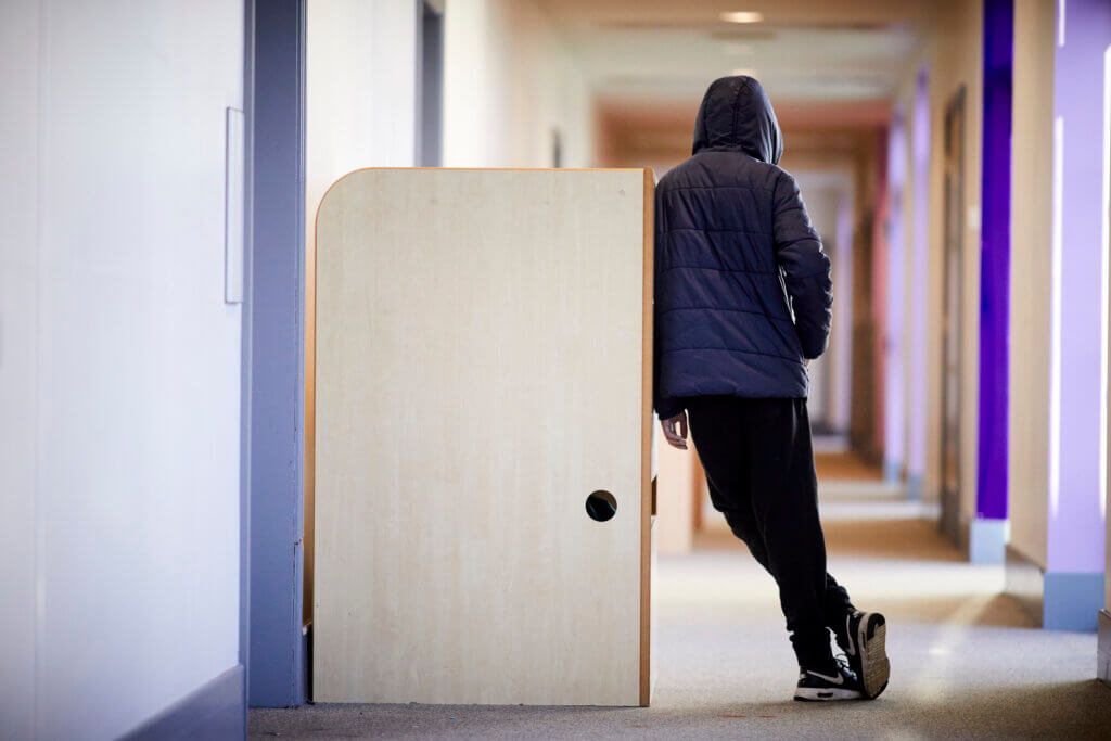 A teenage boy in a school corridor, leaning against a cabinet.