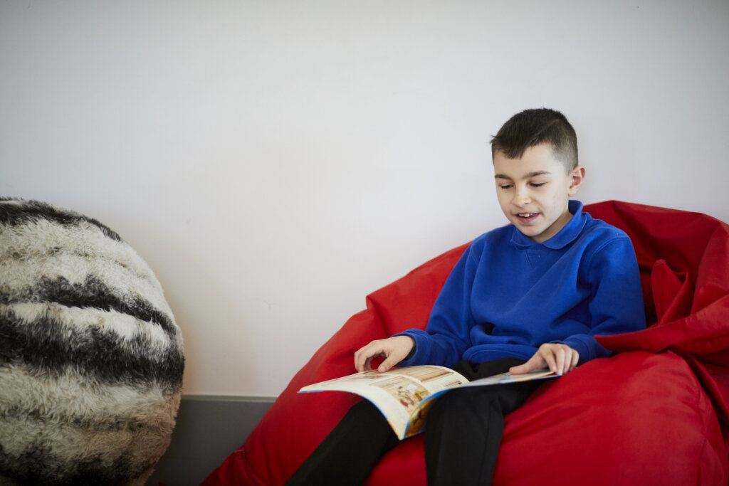 A boy sitting in a beanbag, reading a book.