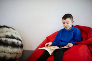 A boy sitting in a beanbag, reading a book.