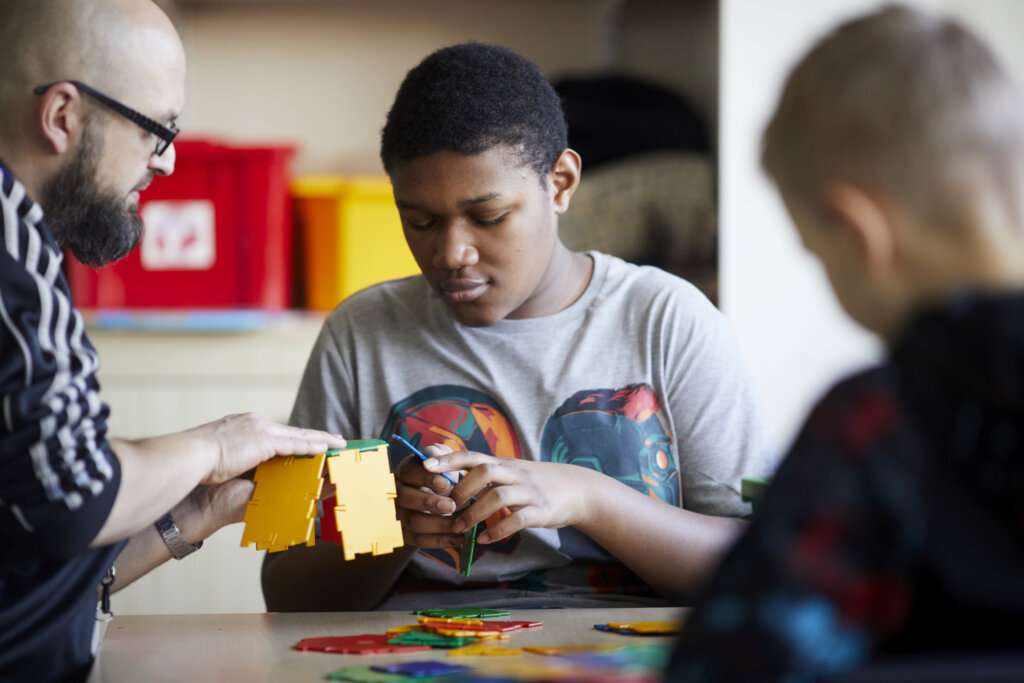 A student putting together a toy structure whilst his teacher helps.