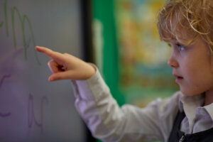 A young girl pointing at an interactive whiteboard.