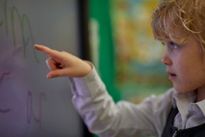 A young girl pointing at an interactive whiteboard.