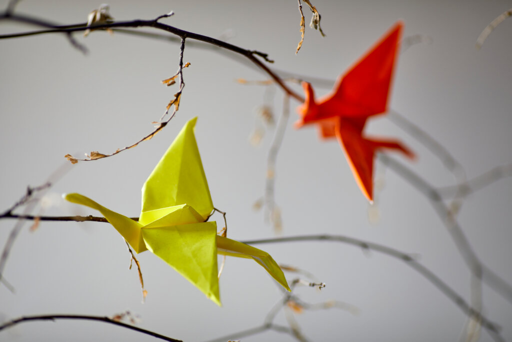 Two paper origami birds, one red and the other yellow, hanging from a tree branch.