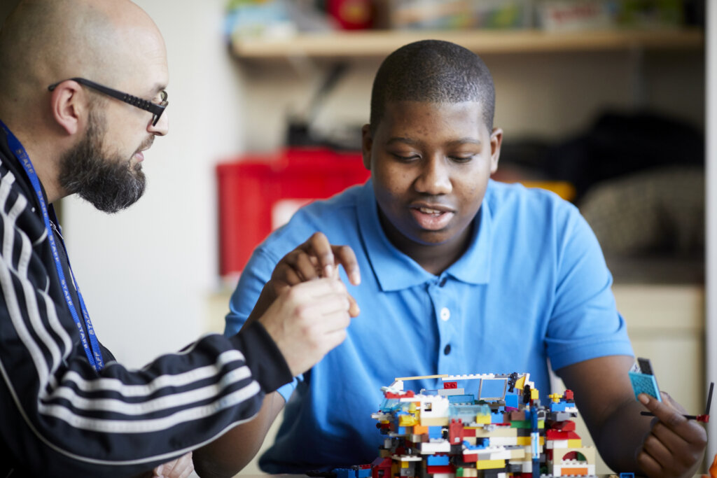 A teacher and pupil building a structure out of lego together.