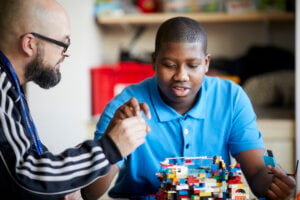 A teacher and pupil building a structure out of lego together.