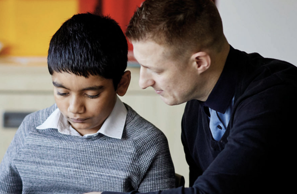 A teacher helps a young boy with his school work