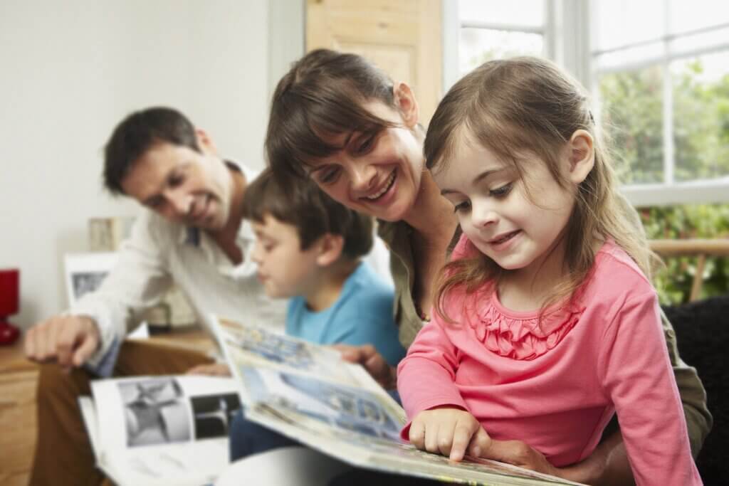 A mum and dad reading books to their young son and daughter.
