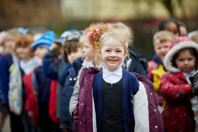 Children lining up in the playground, with a young girl smiling at the front.