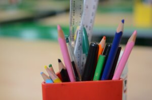 A red pot full of coloured pencils, pens and rulers.