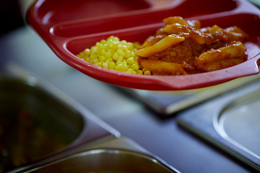 A picture of a school dinner of pasta and sweetcorn on a plastic red tray.
