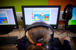 A girl wearing headphones, playing a game on a computer.