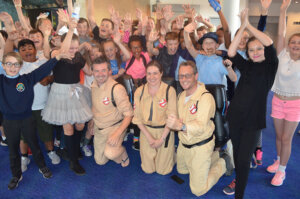 School children cheering, dressed up in 80s costumes with school staff dressed as ghostbusters.