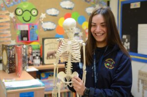 A teacher holds a human skeleton model as she delivers a lesson in the classroom.