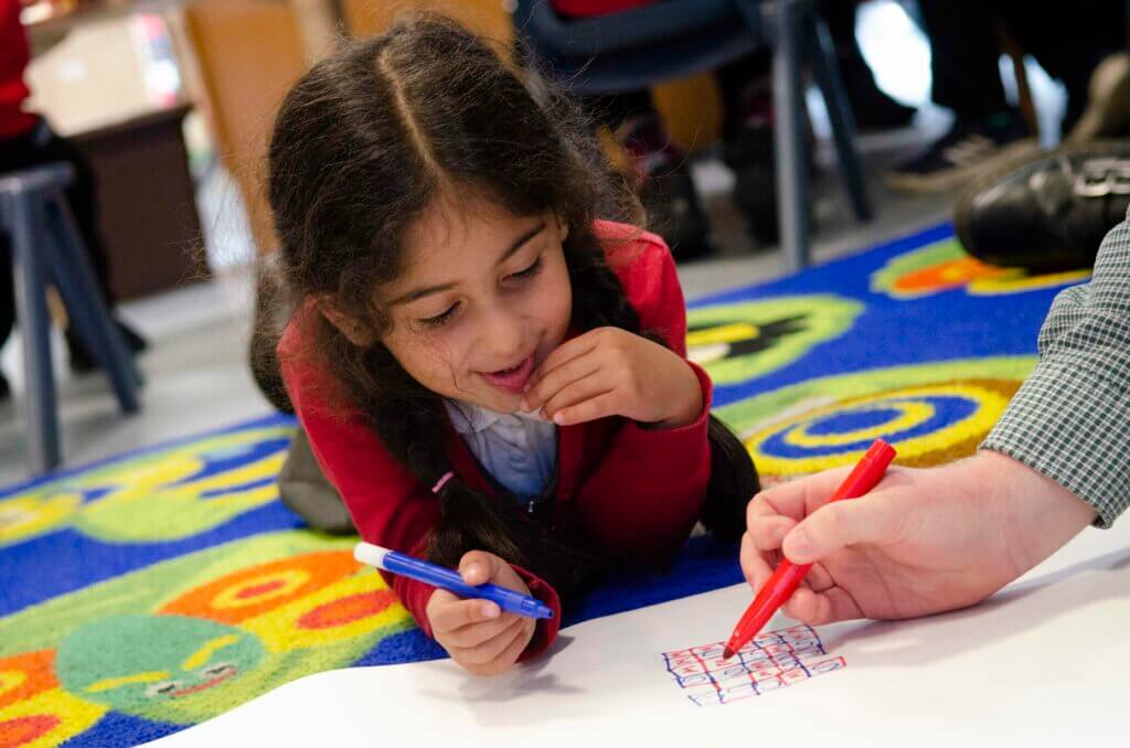 Girl pupil wearing a red jumper, colouring and smiling