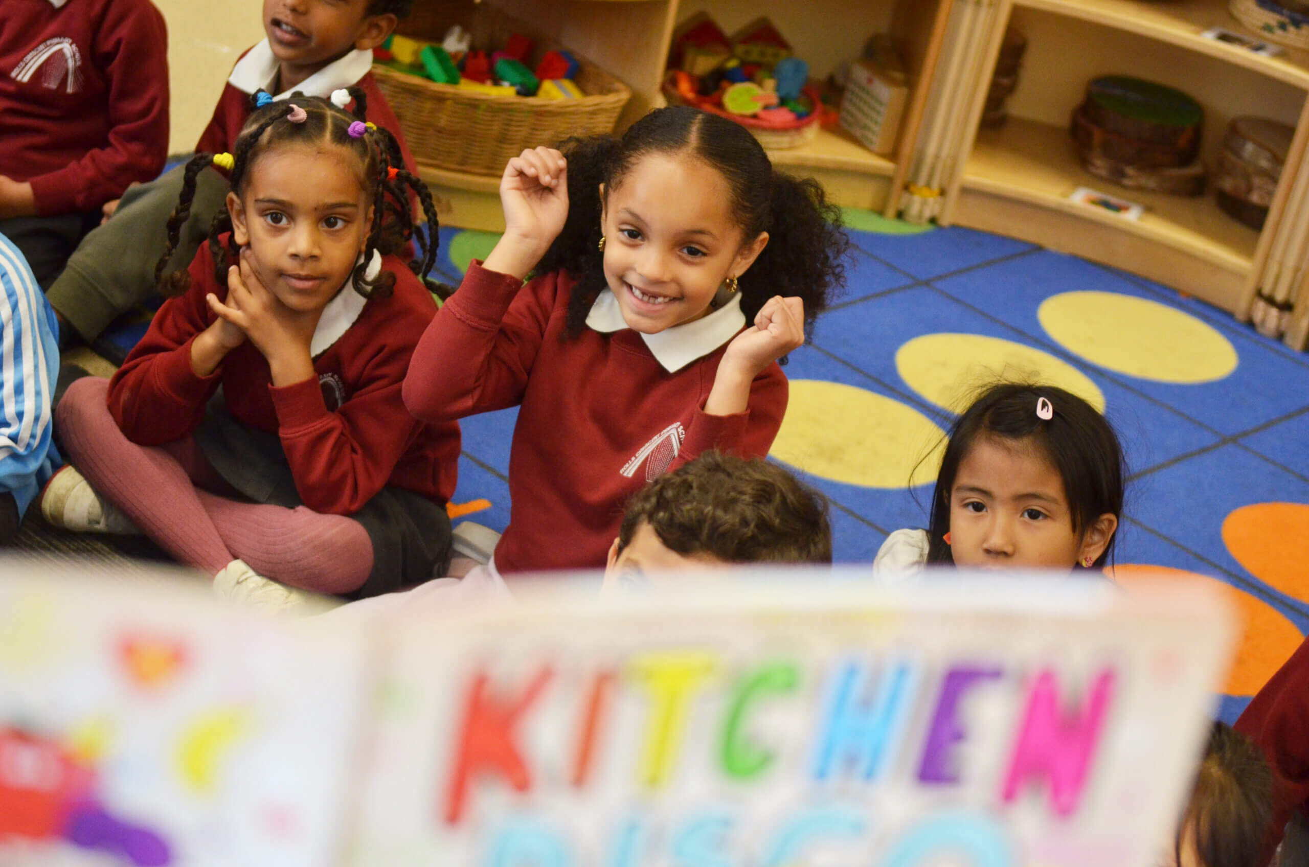 Young children sitting on the carpet in class, as a story is read to them.